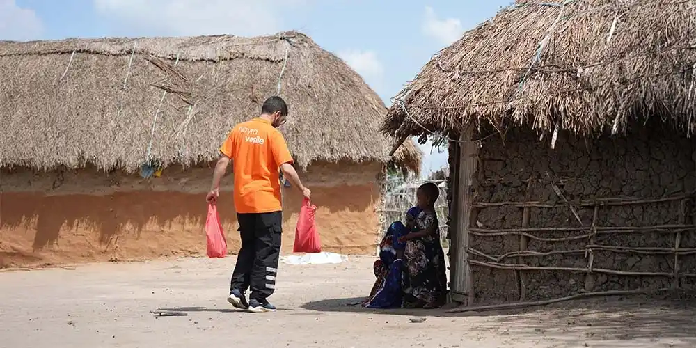 Hayra Vesile görevlisinin Afrika'da bir aileye 'vacip kurban nedir' başlıklı içerik için et poşetlerini götürmesi.